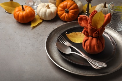 Seasonal table setting with pumpkins and autumn leaves on grey background. Space for text