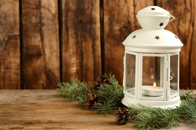 Christmas lantern with burning candle and fir tree branch on wooden background. Space for text