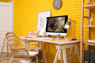 Stylish home office interior with comfortable workplace near yellow brick wall