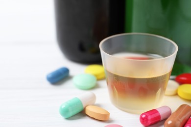 Photo of Measuring cup with syrup, pills on white table, closeup and space for text. Cold medicine