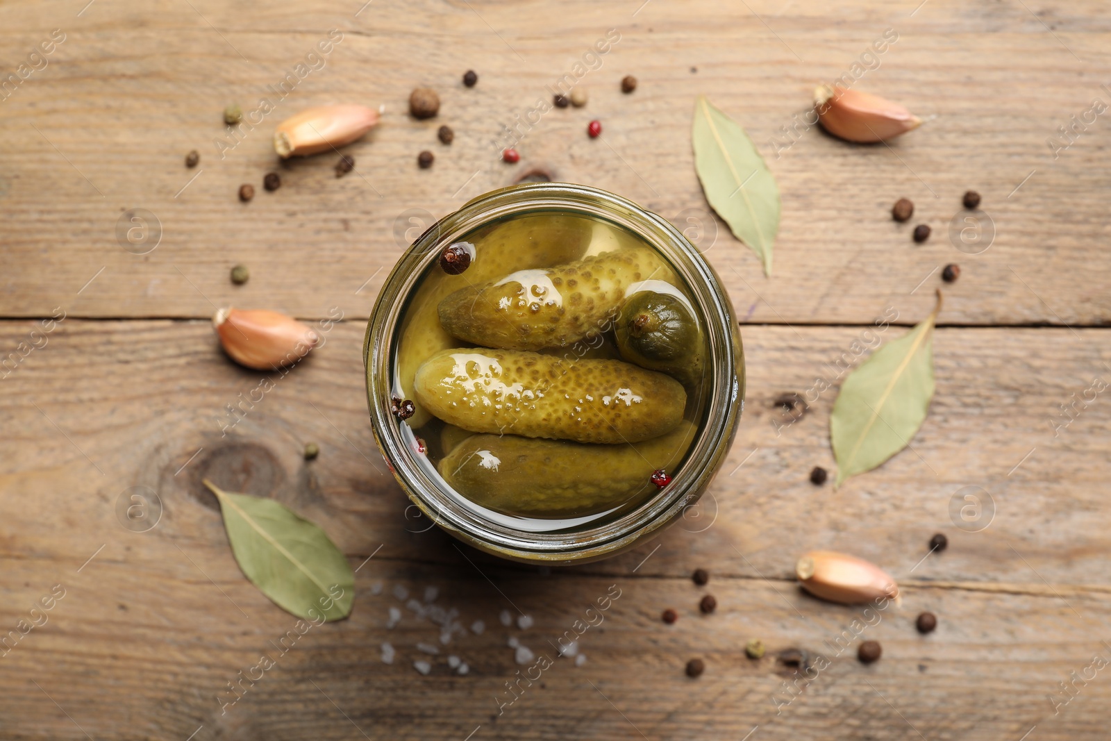 Photo of Tasty pickled cucumbers in glass jar and spices on wooden table, top view