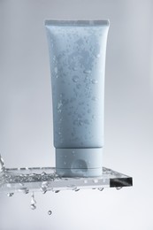 Moisturizing cream in tube on glass with water drops against grey background