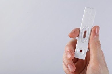 Photo of Woman holding disposable express test on light background, closeup. Space for text