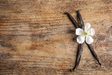 Flat lay composition with aromatic vanilla sticks and flower on wooden background. Space for text