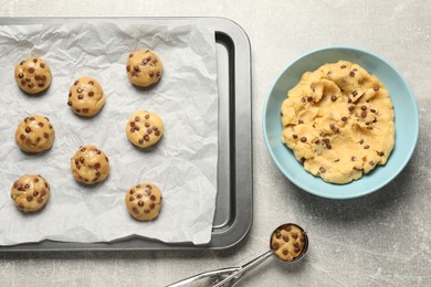 Photo of Bowl with dough and uncooked chocolate chip cookies on light grey table, flat lay