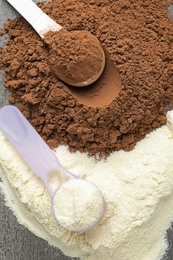 Photo of Piles of different protein powders and scoops on grey table, top view