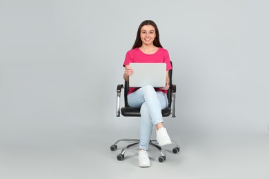 Photo of Young woman with laptop sitting in comfortable office chair on grey background