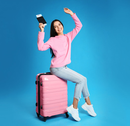 Photo of Beautiful woman with suitcase and ticket in passport for summer trip on blue background. Vacation travel