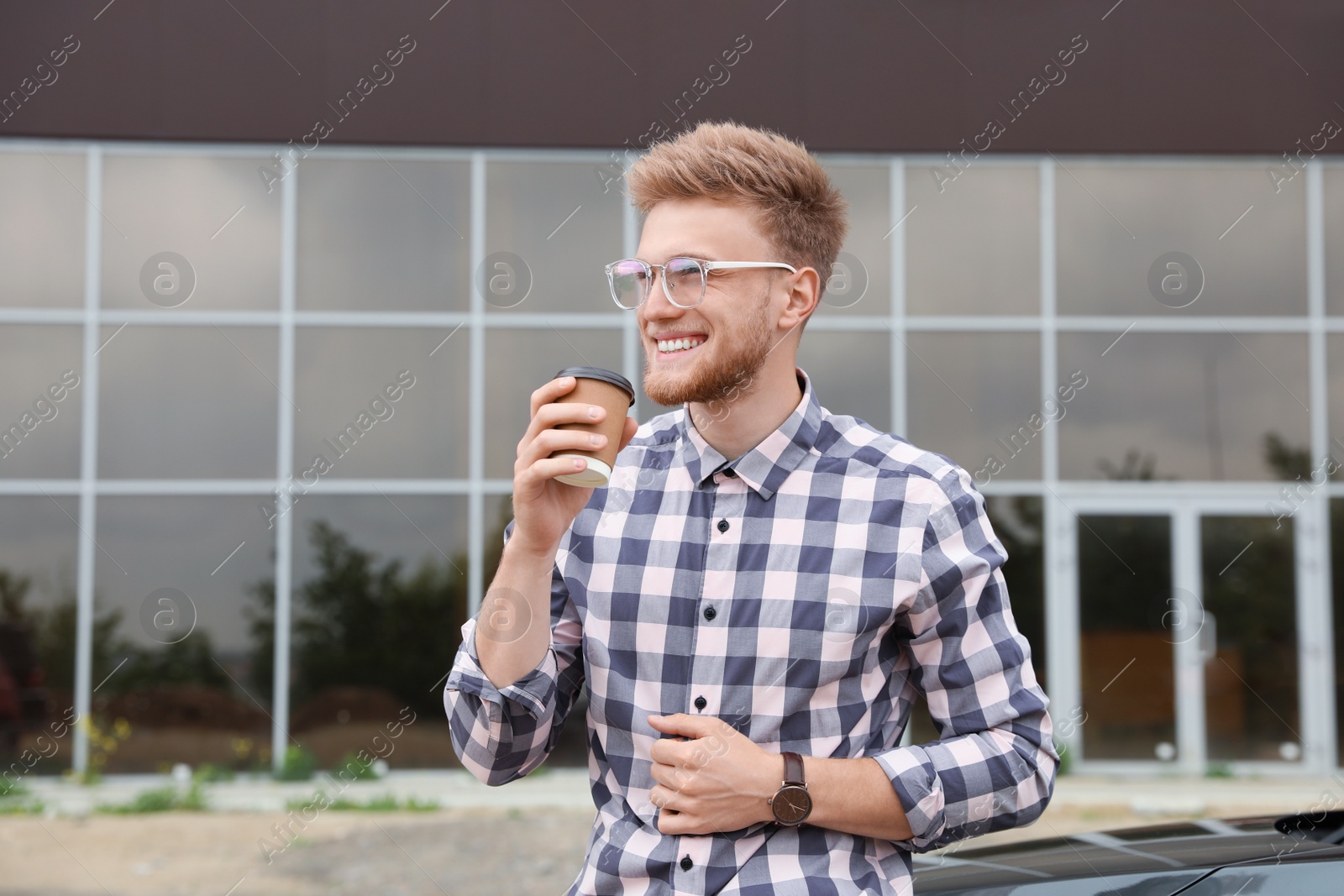 Photo of Attractive young man with cup of coffee near car outdoors