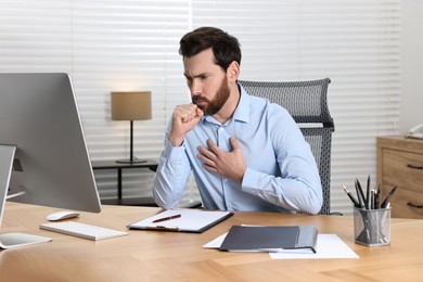 Photo of Sick man coughing at workplace in office. Cold symptoms