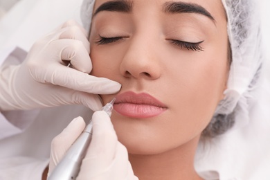 Young woman undergoing procedure of permanent lip makeup in tattoo salon, closeup