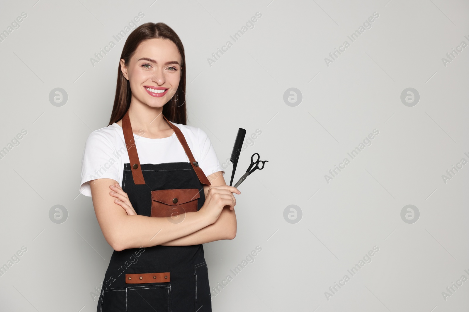 Photo of Portrait of happy hairdresser with comb and scissors on light background. Space for text