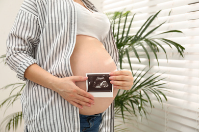 Photo of Pregnant woman with ultrasound photo of her baby at home, closeup