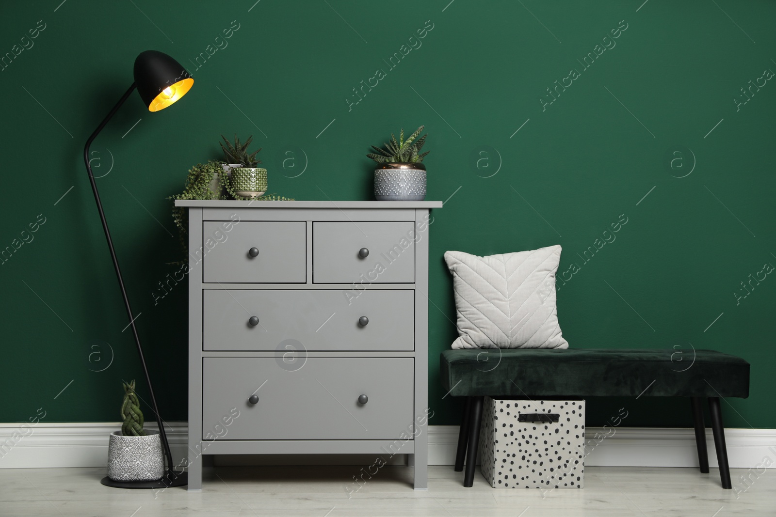Photo of Modern chest of drawers, lamp and comfortable bench near green wall indoors