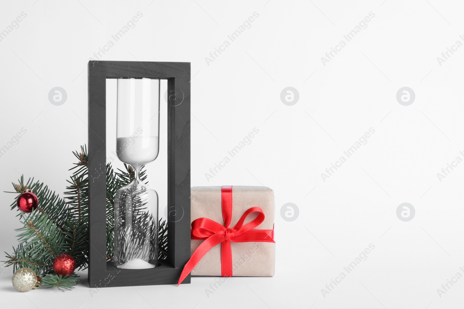 Photo of Hourglass, fir tree branch with decor and present on white background. Christmas countdown