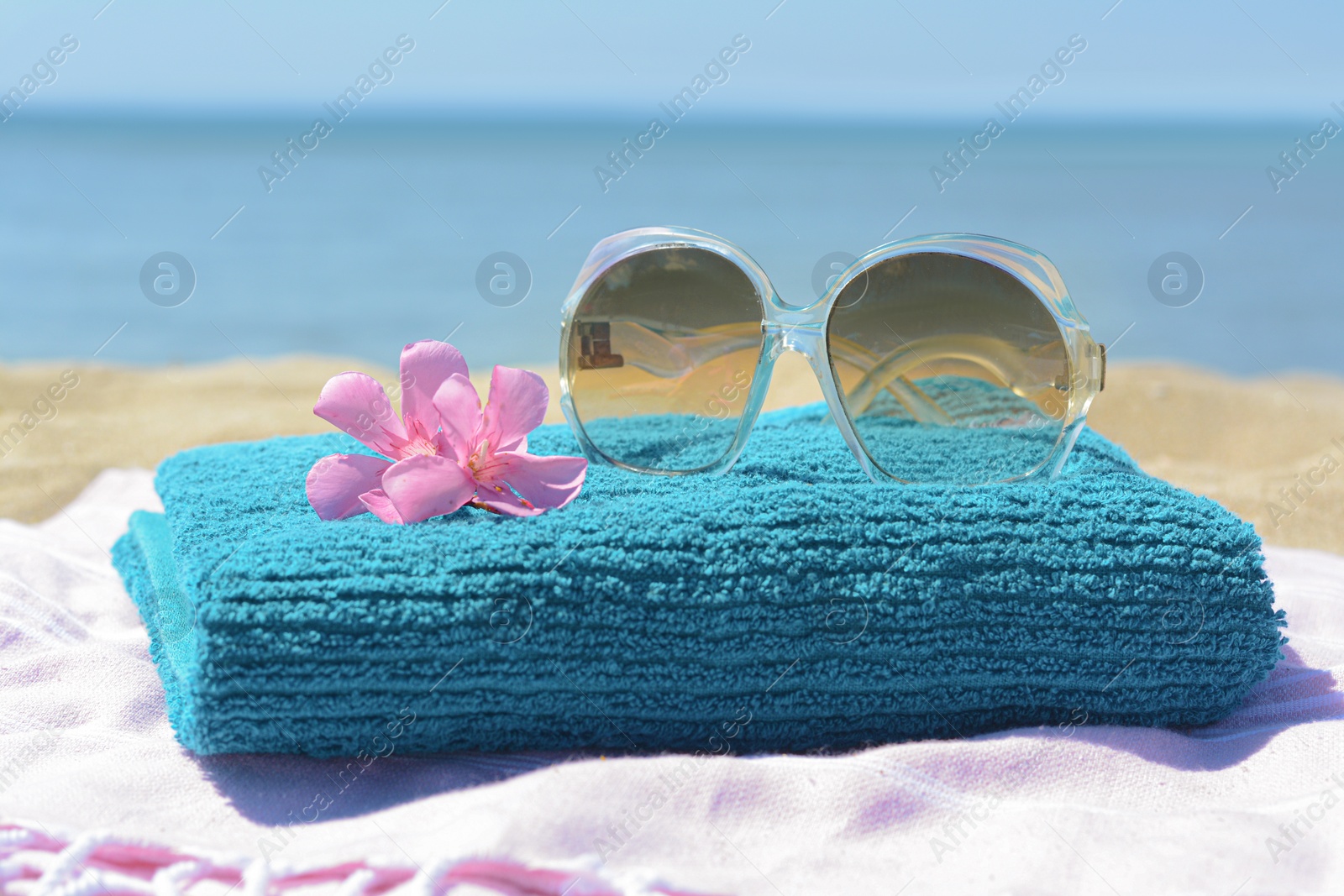 Photo of Blanket with towel, stylish sunglasses and flowers near sea, closeup. Beach accessories