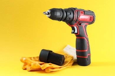 Modern electric screwdriver, battery and gloves on yellow background