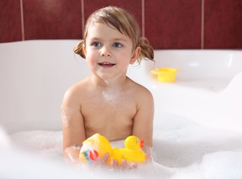 Photo of Smiling girl bathing with toy ducks in tub
