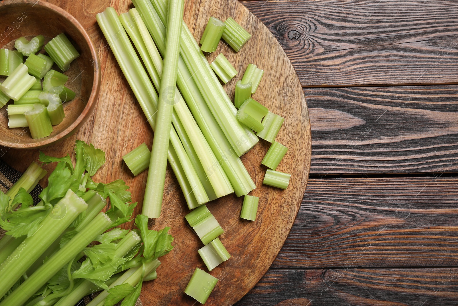 Photo of Board with fresh cut celery stalks on wooden table, top view. Space for text