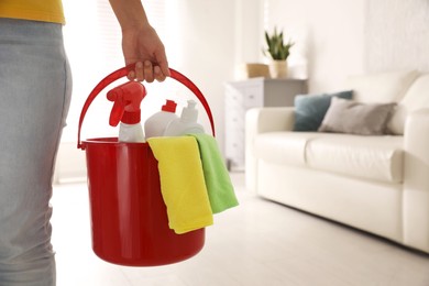 Photo of Woman holding bucket with cleaning supplies in living room, closeup. Space for text