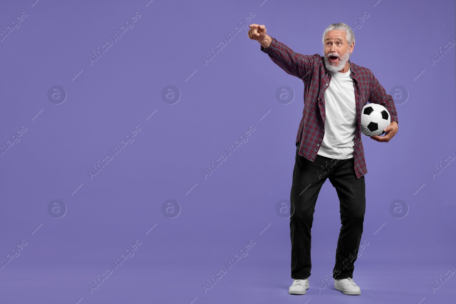 Photo of Emotional senior sports fan with soccer ball on purple background, space for text