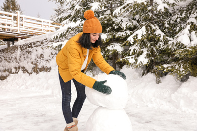 Photo of Happy woman making snowman outdoors. Winter vacation