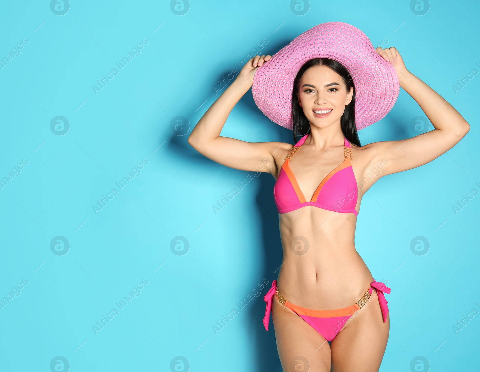 Photo of Beautiful young woman in stylish bikini with hat on light blue background. Space for text