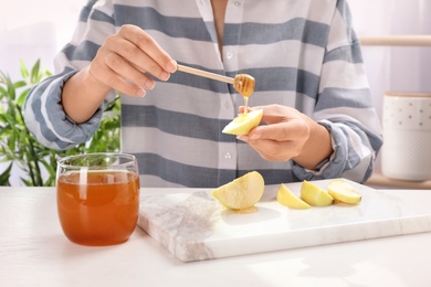 Photo of Woman pouring honey onto sliced apple at table