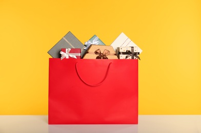 Photo of Paper shopping bag full of gift boxes on yellow background