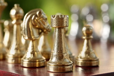Photo of Golden rook and other chess pieces on game board against blurred background, closeup
