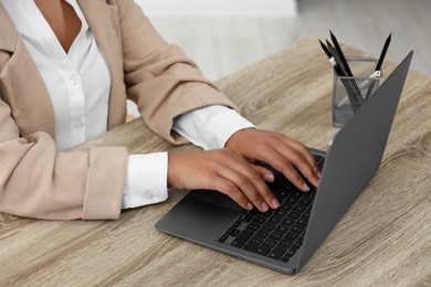 Photo of Woman using laptop at wooden desk indoors, closeup