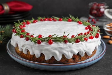 Photo of Traditional Christmas cake decorated with rosemary and cranberries on dark grey table, closeup