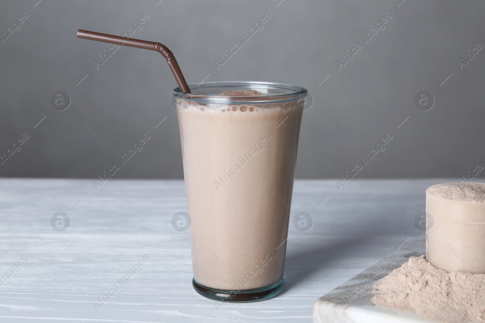 Photo of Glass with protein shake and scoop of powder on white wooden table