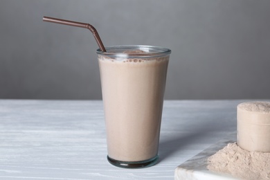 Glass with protein shake and scoop of powder on white wooden table