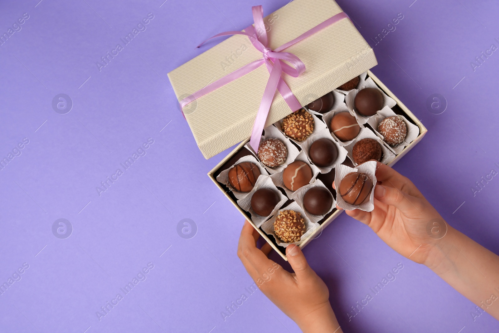 Photo of Child taking delicious chocolate candy from box on light purple background, top view. Space for text