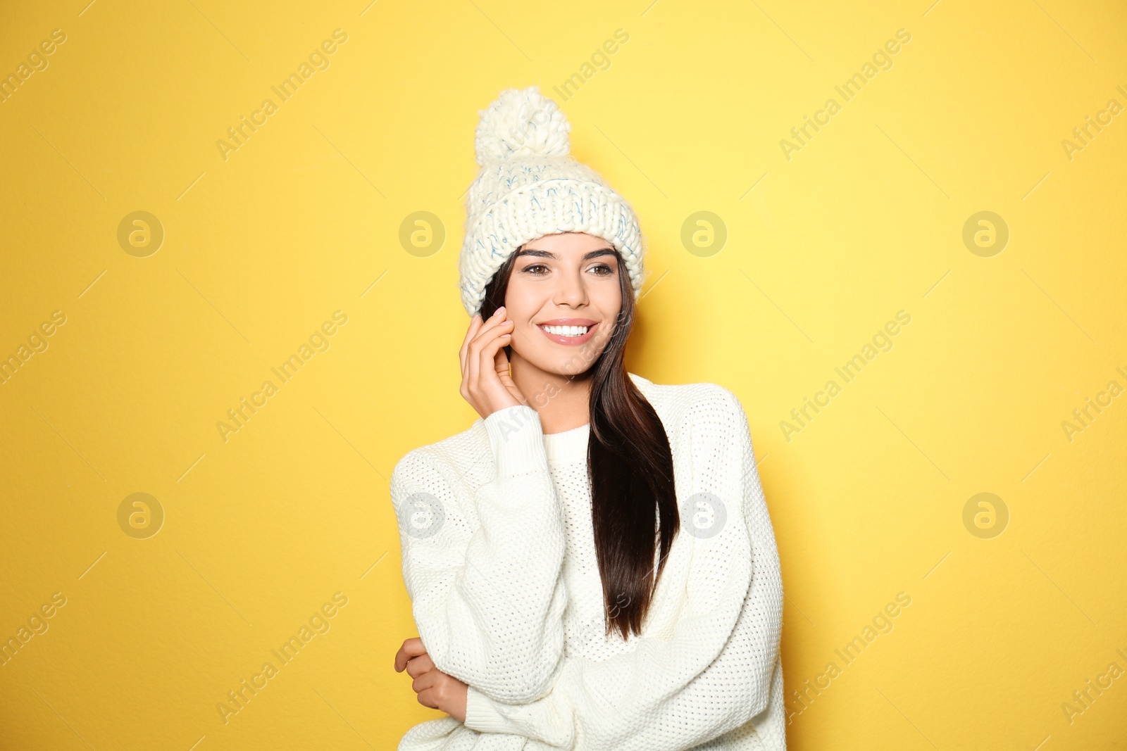 Image of Happy young woman wearing warm sweater and knitted hat on yellow background
