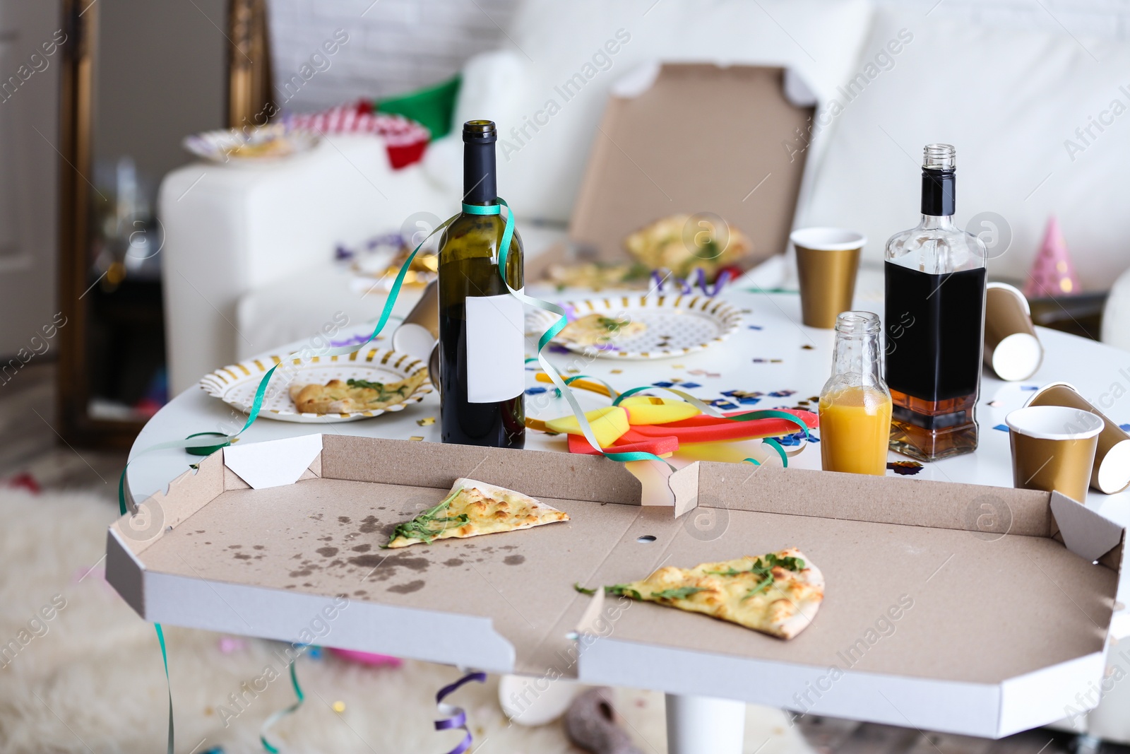 Photo of Messy table with bottles and pizza indoors. Chaos after party