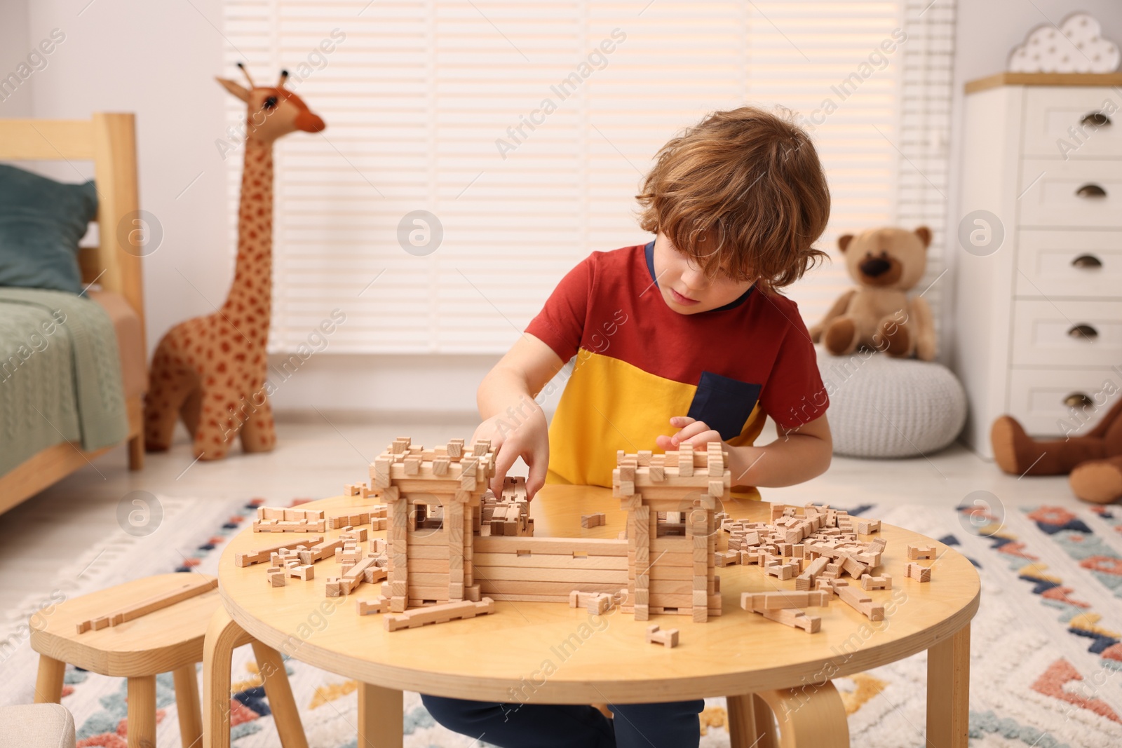 Photo of Little boy playing with wooden entry gate at table in room. Child's toy