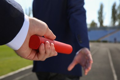 Photo of Businessman passing baton to his partner outdoors, closeup