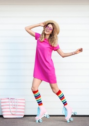 Happy young woman with retro roller skates near white garage door