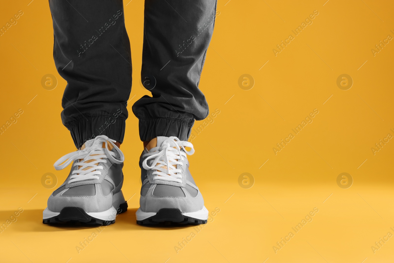 Photo of Man wearing stylish sneakers on yellow background, closeup. Space for text