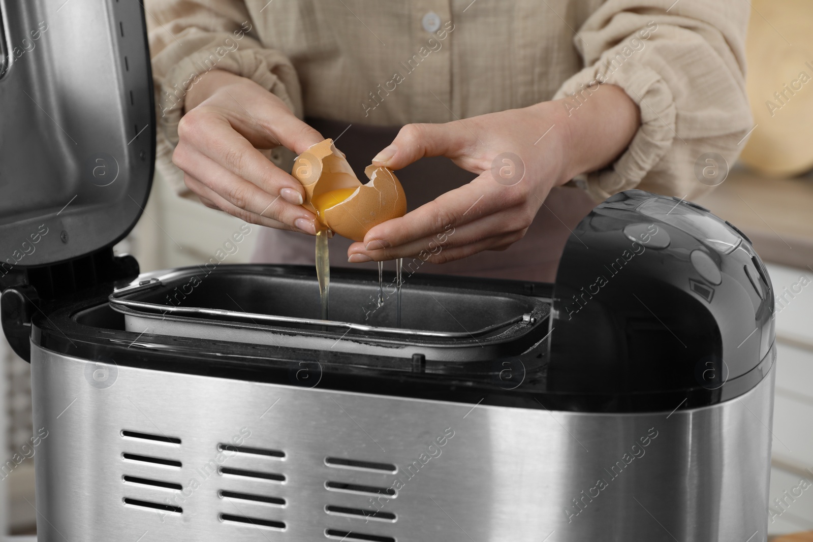 Photo of Making dough. Woman breaking egg into breadmaker pan, closeup