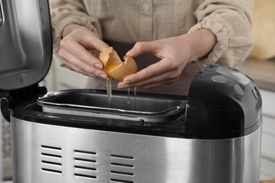 Making dough. Woman breaking egg into breadmaker pan, closeup