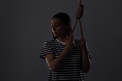 Depressed woman with rope noose on grey background