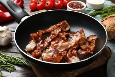 Photo of Delicious bacon slices in frying pan and products on wooden table, closeup