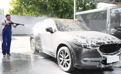 Photo of Young worker cleaning automobile with high pressure water jet at car wash