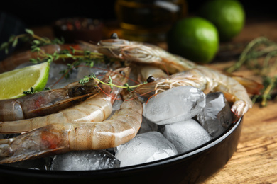 Photo of Fresh raw shrimps with ice on wooden table, closeup