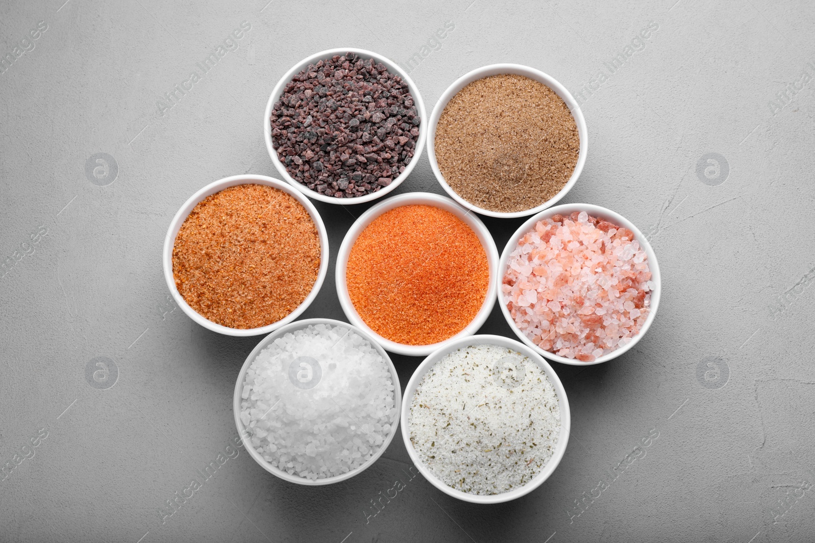 Photo of Different kinds of salt on light grey table, flat lay