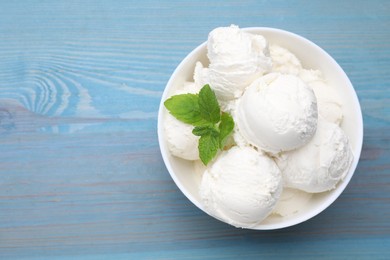 Photo of Delicious vanilla ice cream and mint in bowl on light blue wooden table, top view. Space for text
