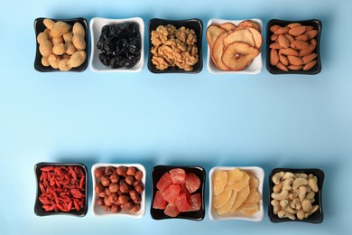 Bowls with dried fruits and nuts on light blue background, flat lay. Space for text